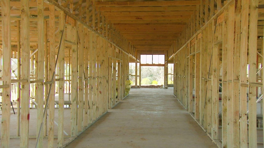 An internal view of a long house being built with wooden framework on a concrete slab.