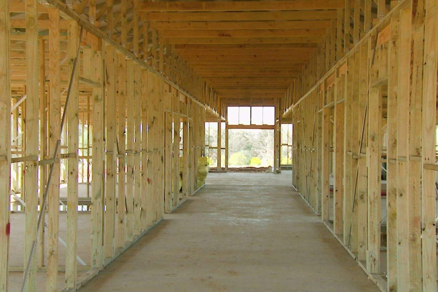 An internal view of a long house being built with wooden framework on a concrete slab.