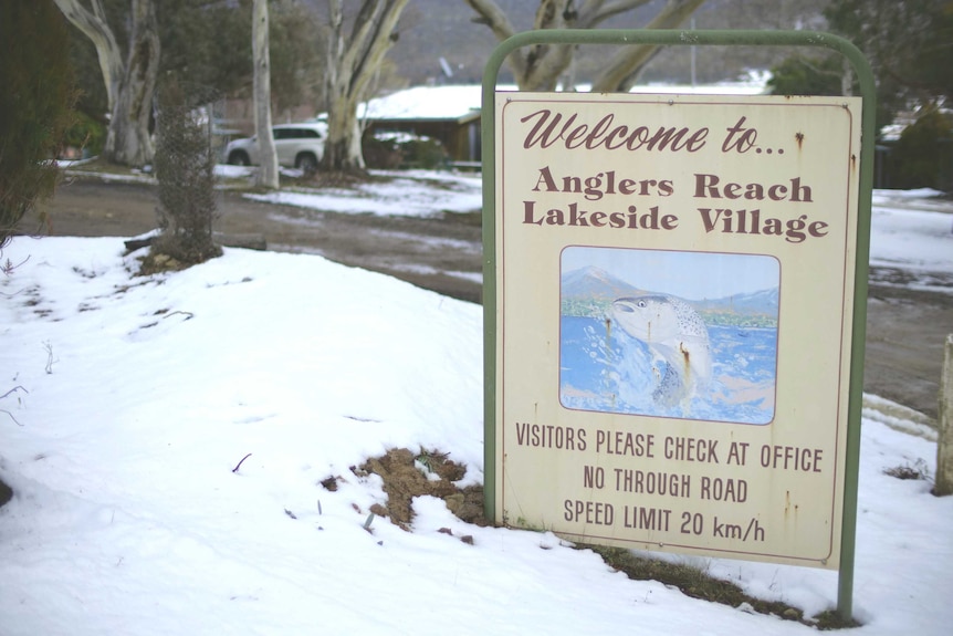 A sign next to a road reads "Welcome to … Anglers Reach Lakeside Village". There is snow all over the ground.