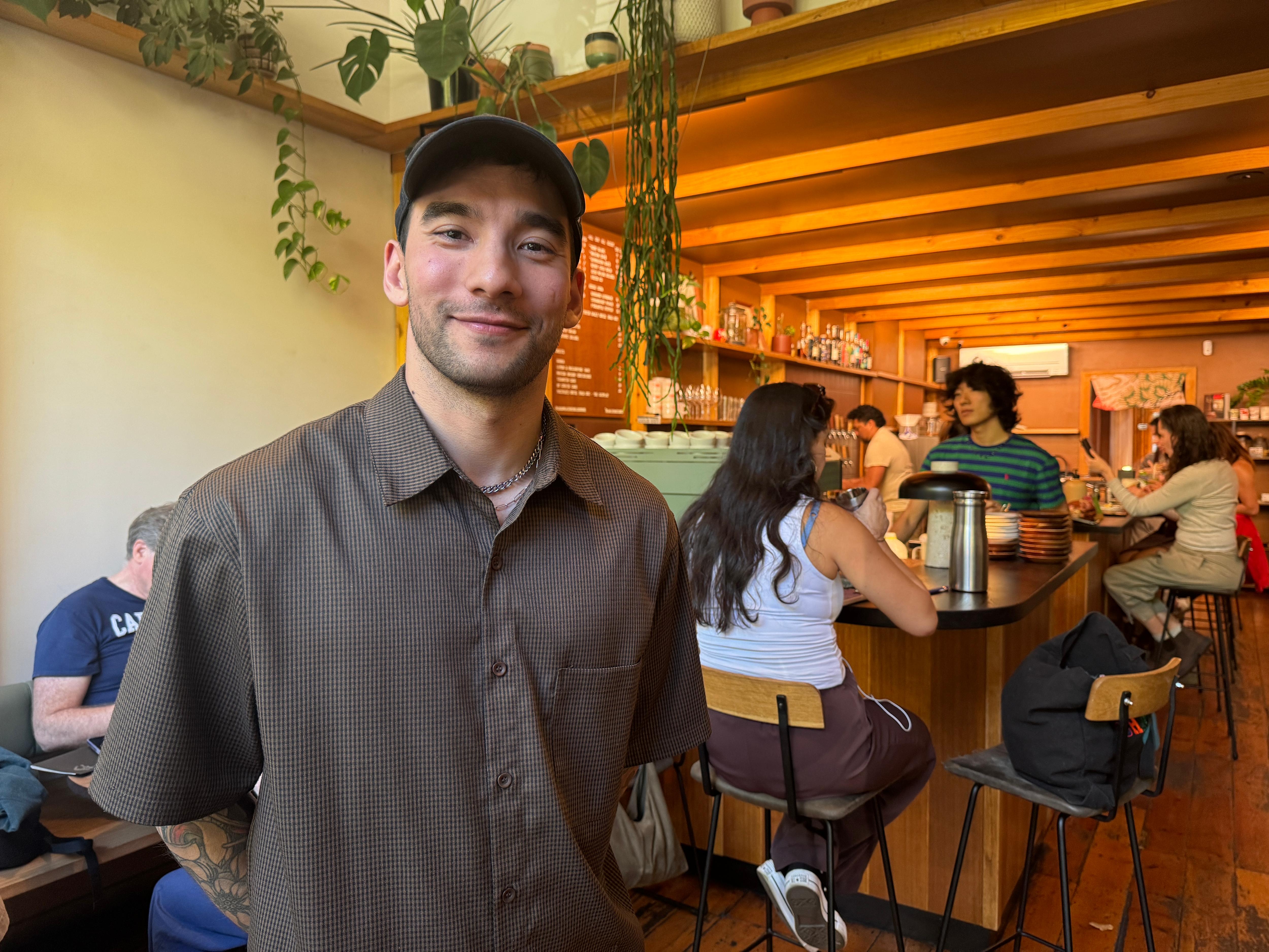 Un hombre con camisa y gorra se encuentra frente a la cafetería.