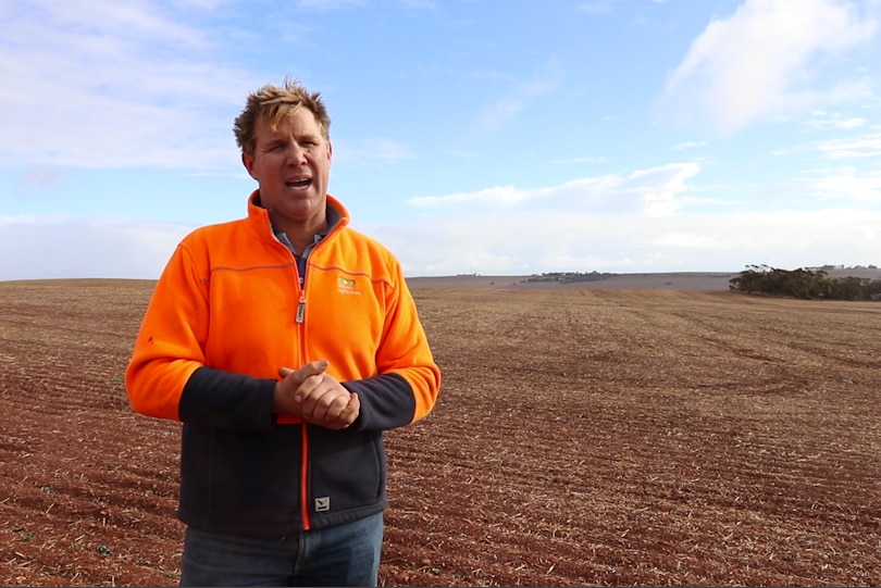 Man wearing high visibility clothing standing in a dry paddock with blue sky in the background.