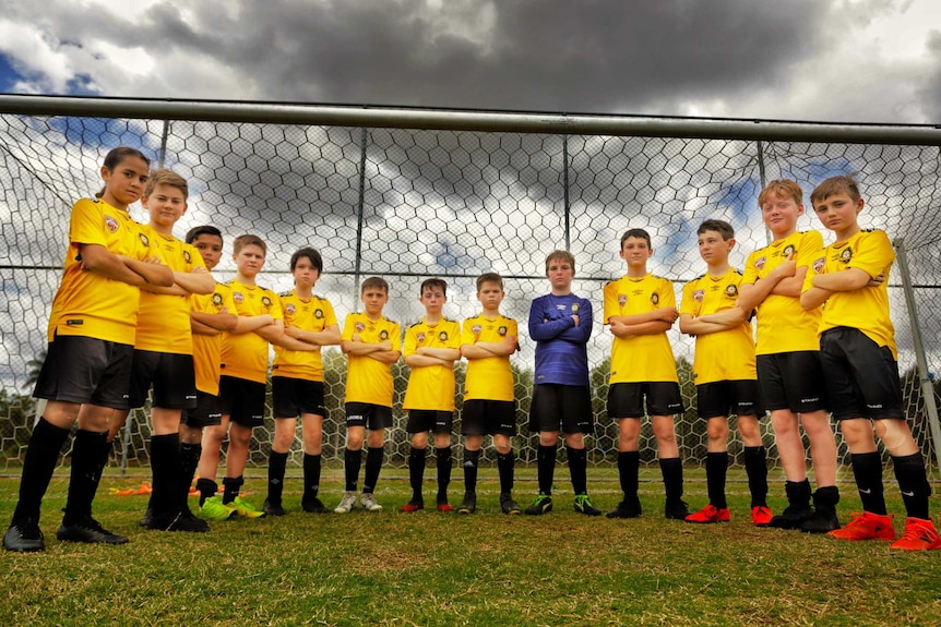 A young sports team stands frowning in front of a soccer goal.