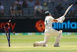 Bails come off stumps as a cricket ball hits them behind Australia batter David Warner, who is completing a stroke.