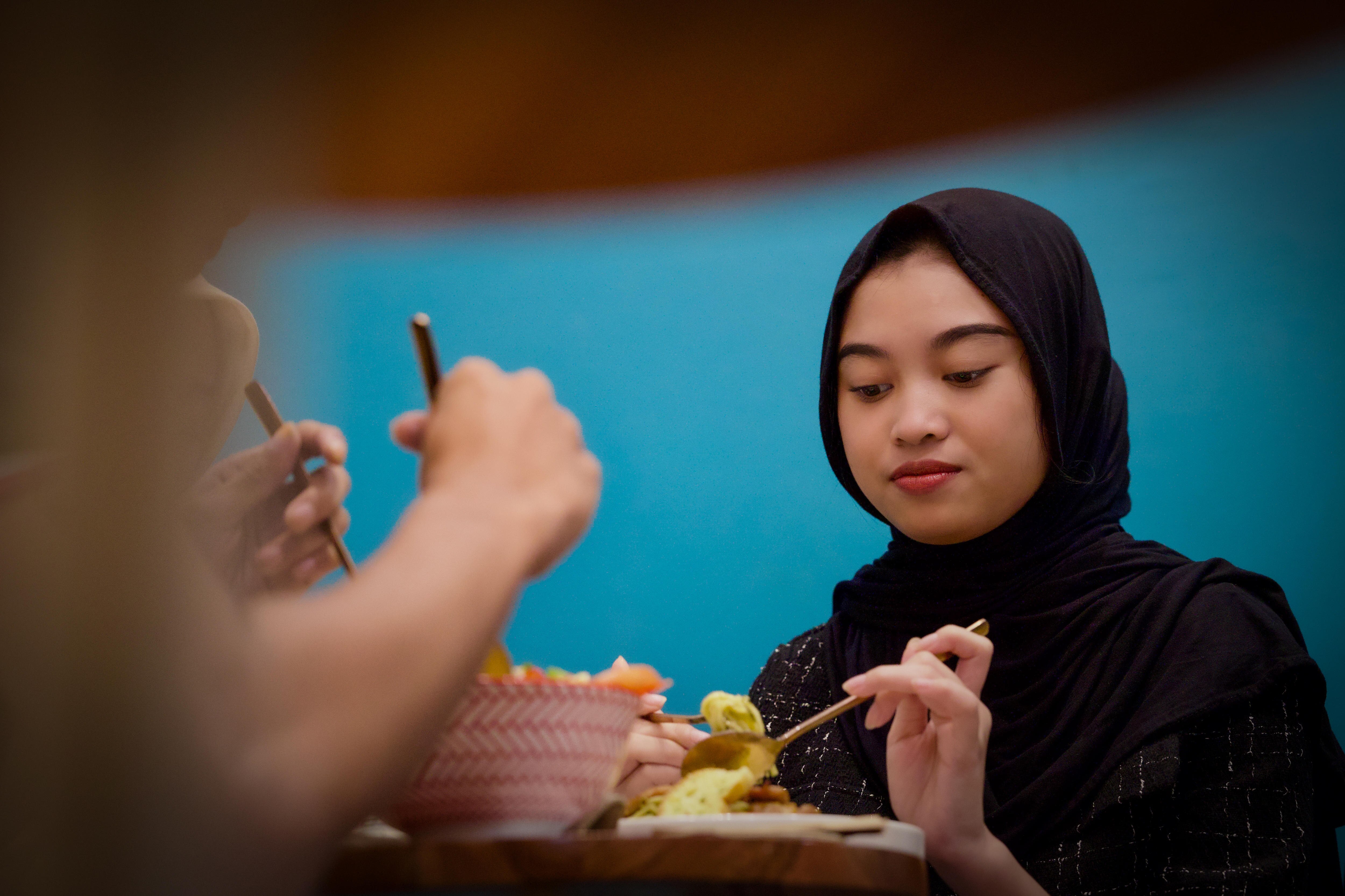 A woman wearing a hijab looks down as she paints a pot.
