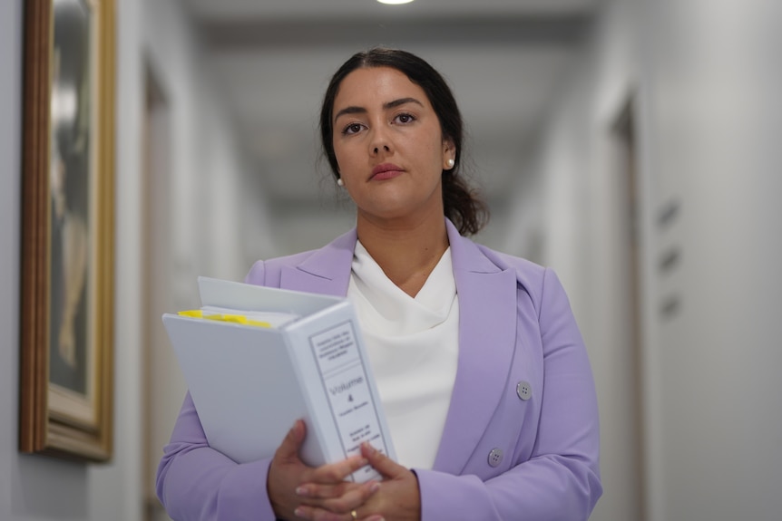 A woman holds a large white folder of documents