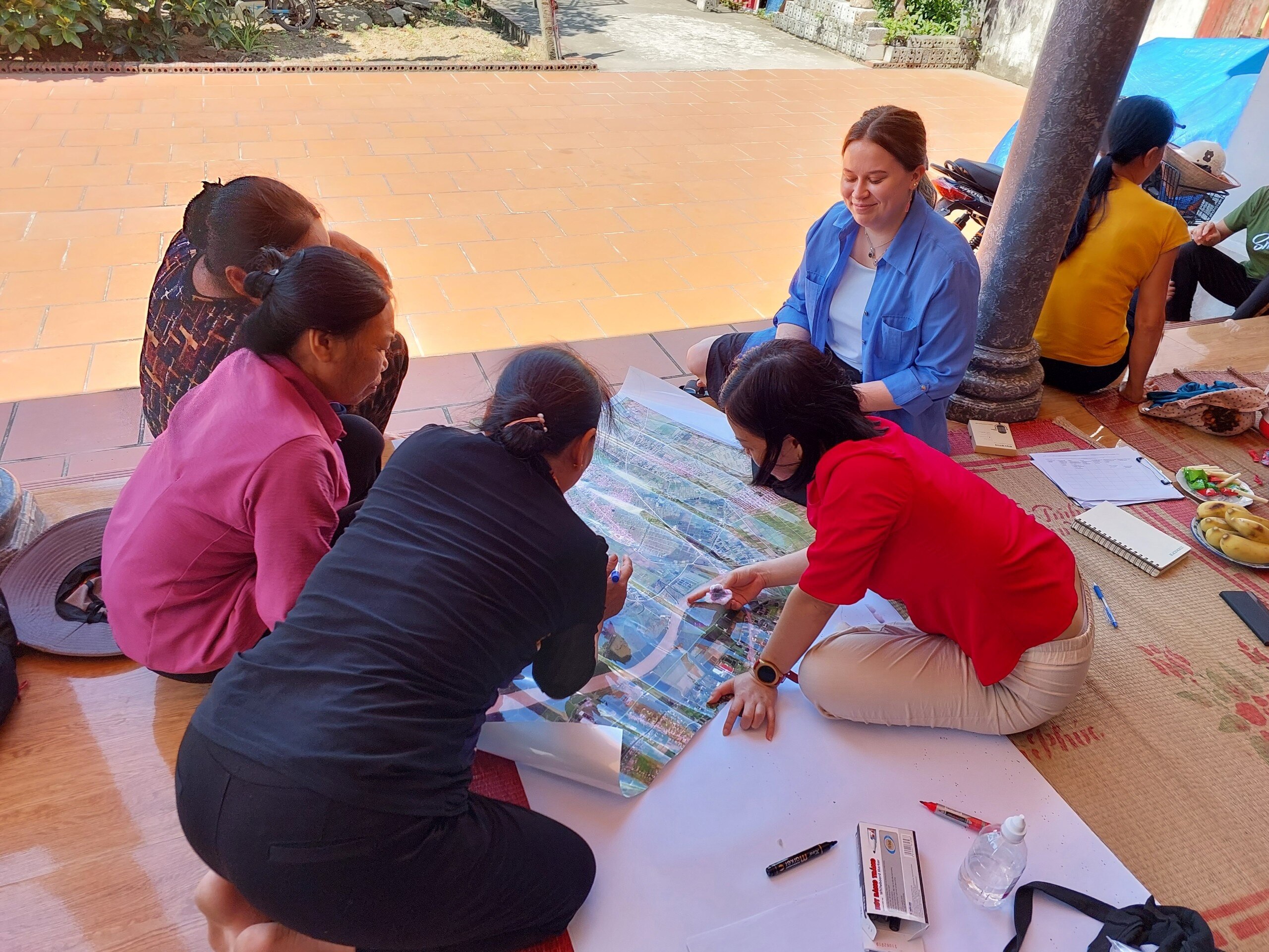 A PhD researcher sits with Vietnam locals, surveying a large map laid out on the floor.