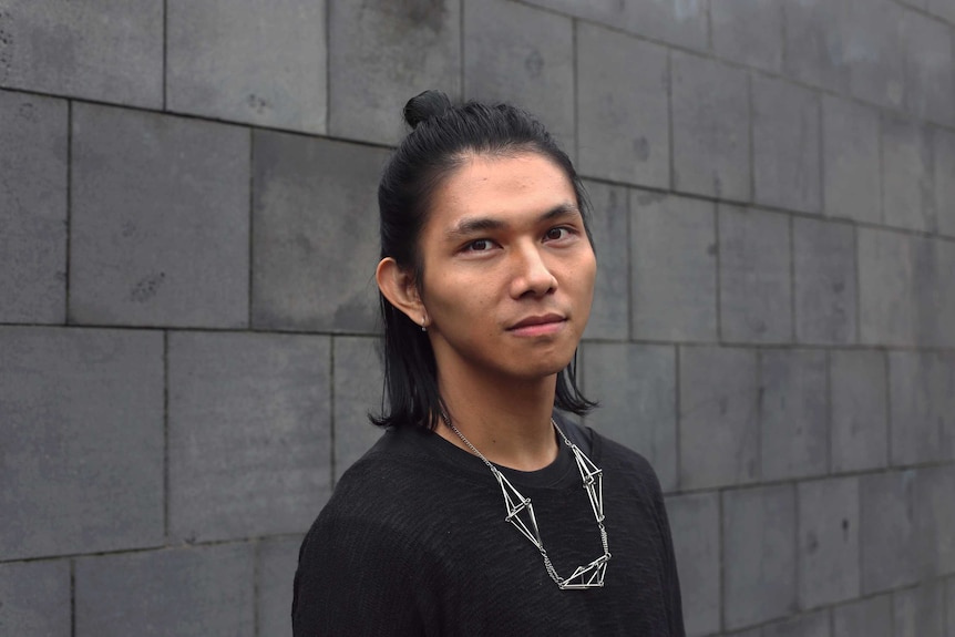 Headshot of a young man with a bun and interesting jewellery