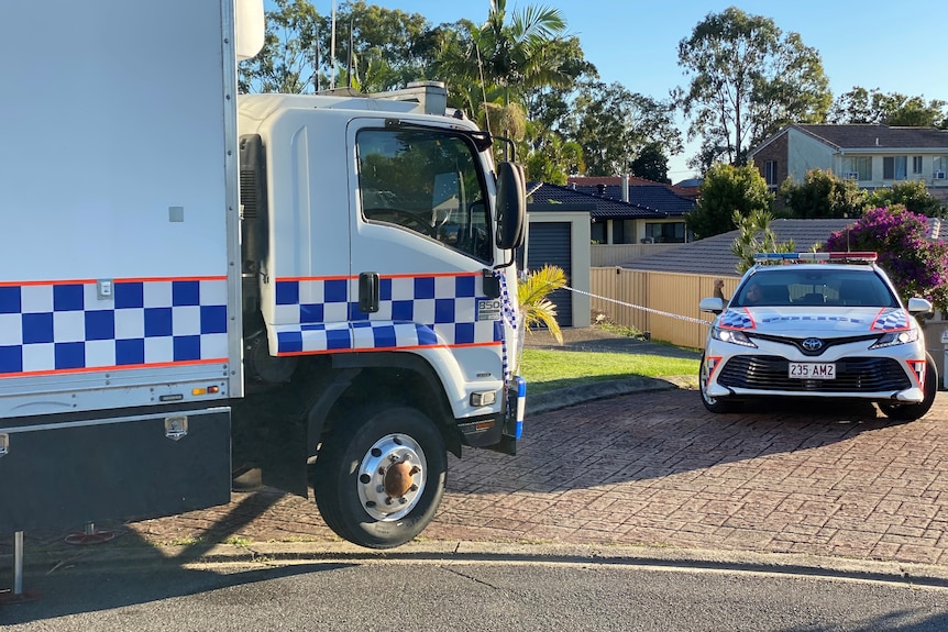 A police van and car outside a one-storey brick home. Police tape covers the driveway.