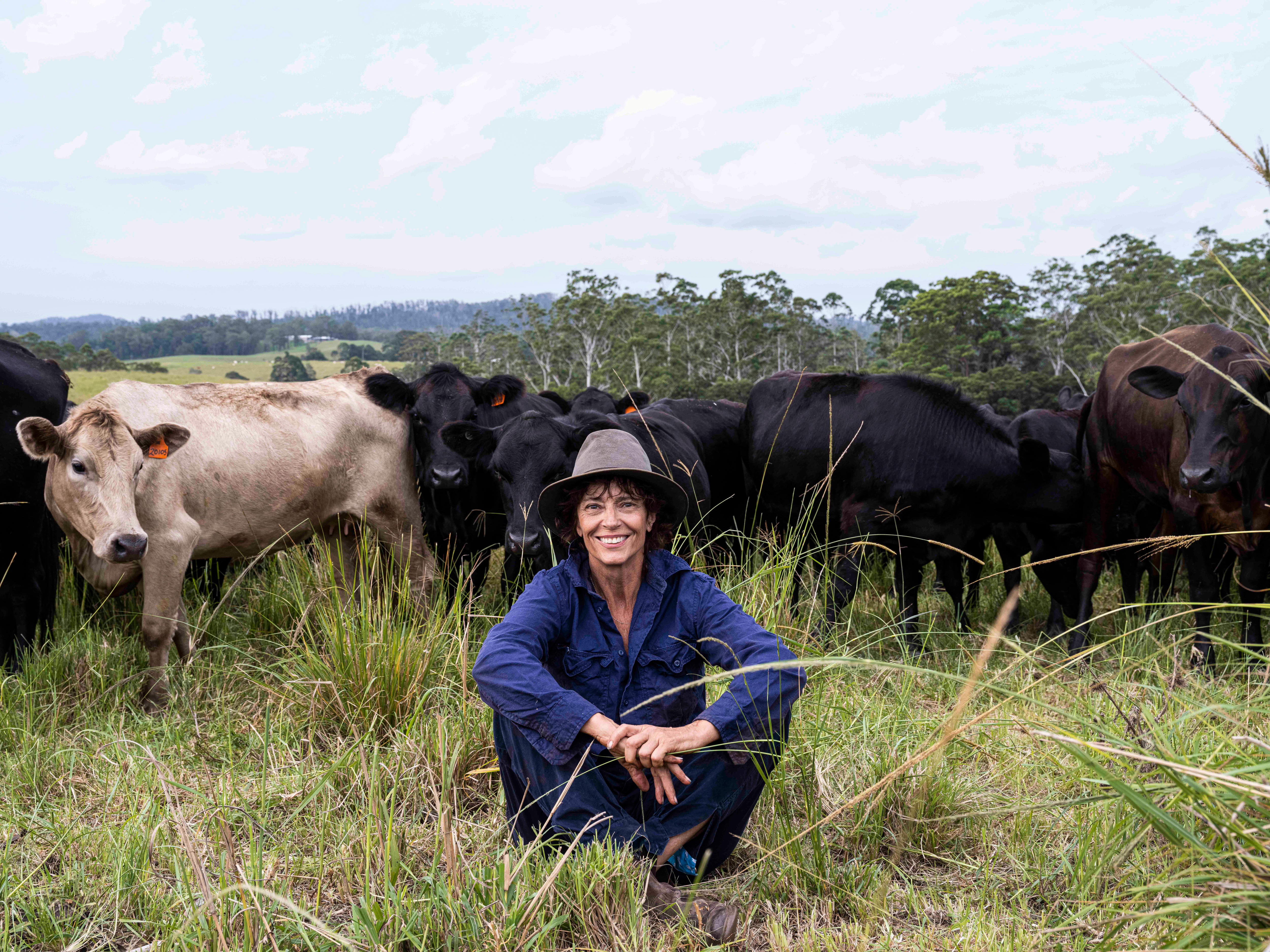 A woman sits in a pasture with cows behind her.
