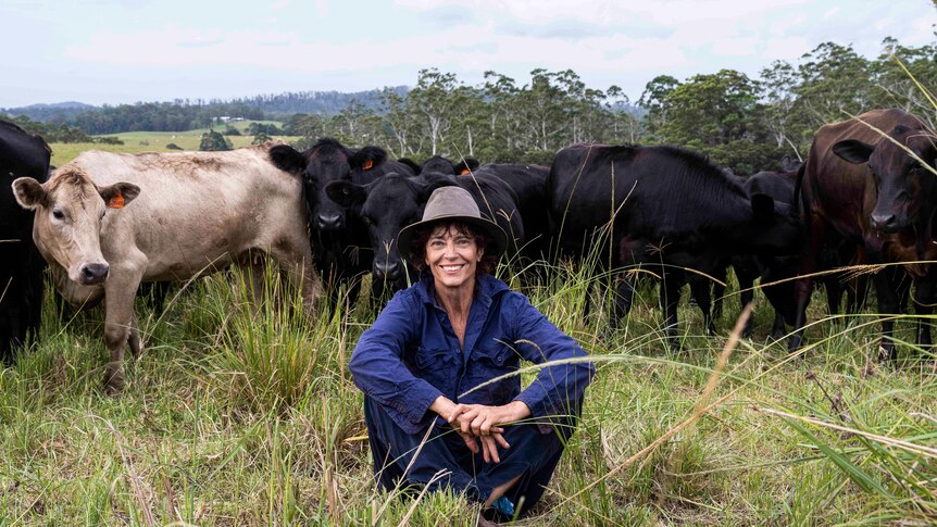A woman sits in a pasture with cows behind her.