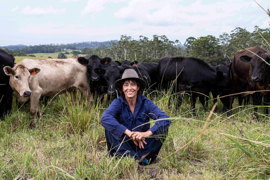 A woman sits in a pasture with cows behind her.