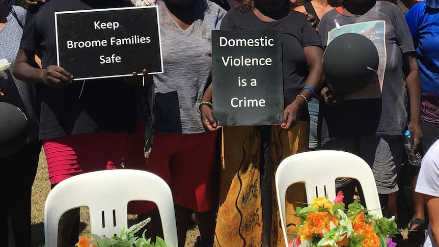 Flowers in memory of lost ones sit in front of unidentified women holding signs