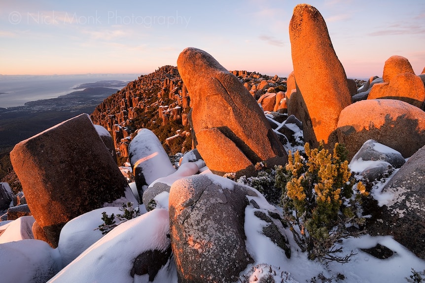 A rocky mountain top dusted with snow, lit from the side