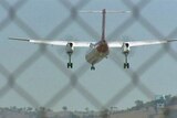 A twin-prop plane flies behind a chainlink fence