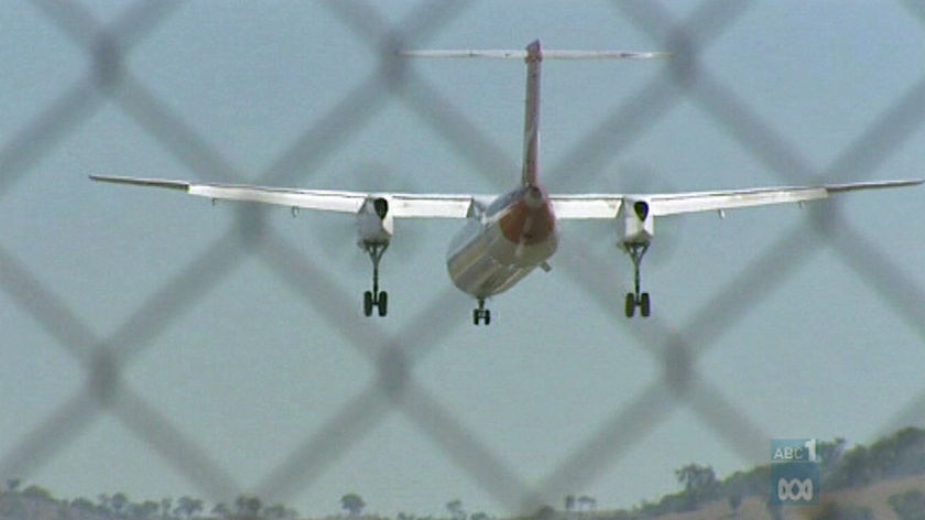 A twin-prop plane flies behind a chainlink fence