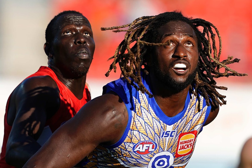 A West Coast Eagles AFL player stands in front of a Sydney Swans opponent as they watch the ball in the air.