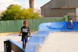 A young boy riding a scooting on a wavy blue circuit track. 