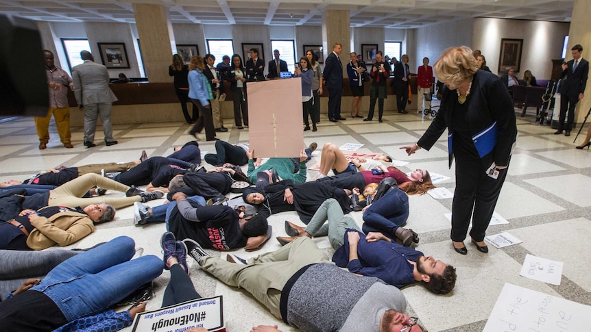 A group of students lie on the floor with signs denouncing loose gun controls