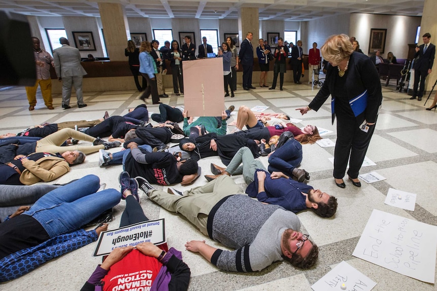 A group of students lie on the floor with signs denouncing loose gun controls