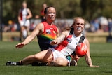 Daisy Pearce slides behind Tilly Lucas-Rodd with an AFL ball bouncing in front of them