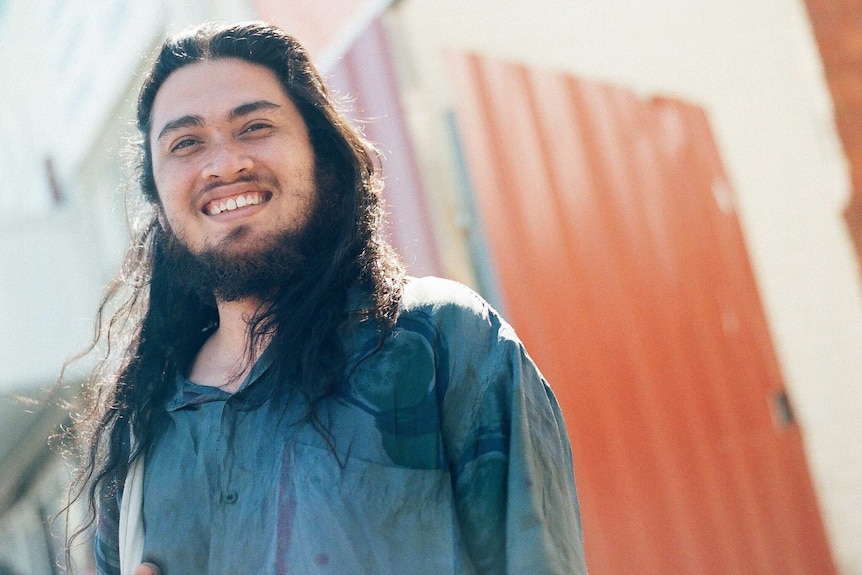 The artist, a young man, smiles and poses for the camera.