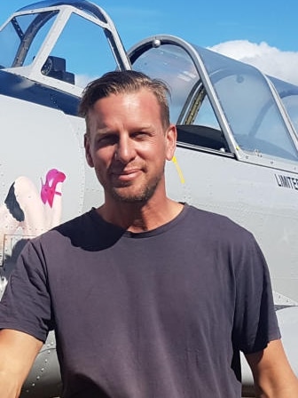 Young man smiling stands in front of a plane.