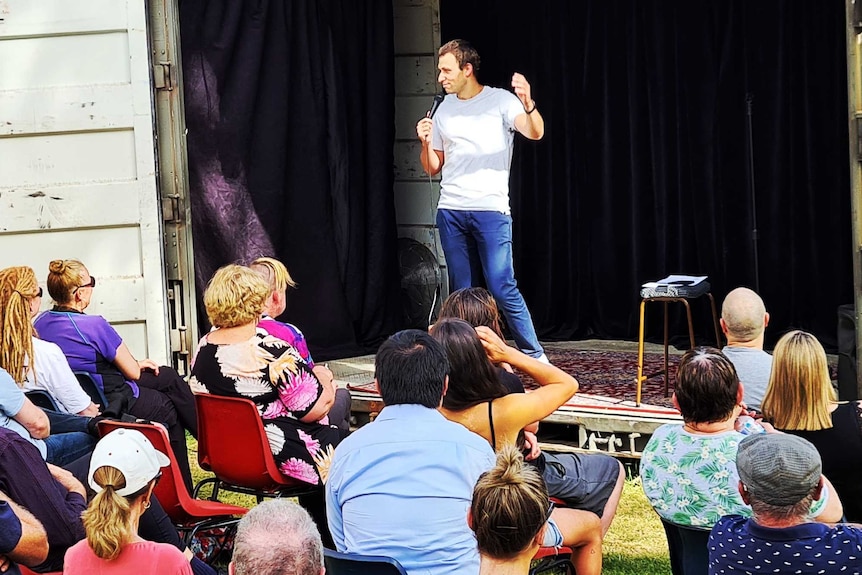 A man performs to a small audience from a small makeshift stage.