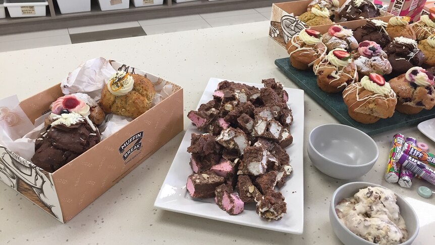 Different muffins in Muffin Break boxes, next to a platter of rocky road, a bowl of ice cream and life saver lollies