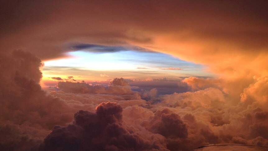 View from a small plane, with part of the wing in view, of the late afternoon sun lights up an opening in the clouds.