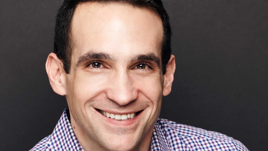 Headshot portrait of man with dark hair and dark eyes smiling at camera