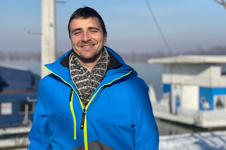 A man in a bright blue windbreaker smiles at the camera