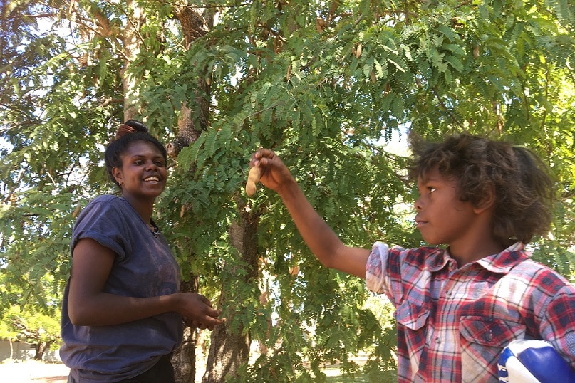 Two children stand by a tree in Woodicupildiya.