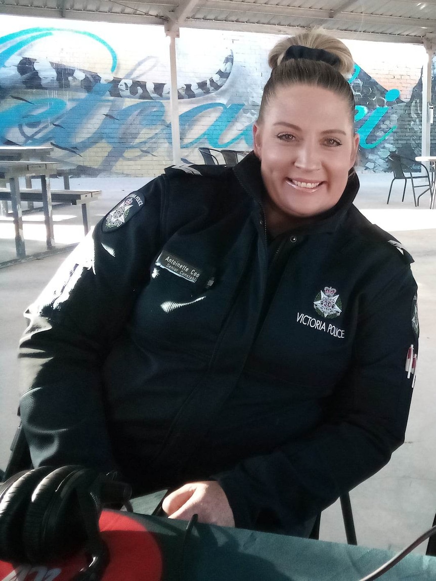 A policewoman smiles in front of a mural of a snake.