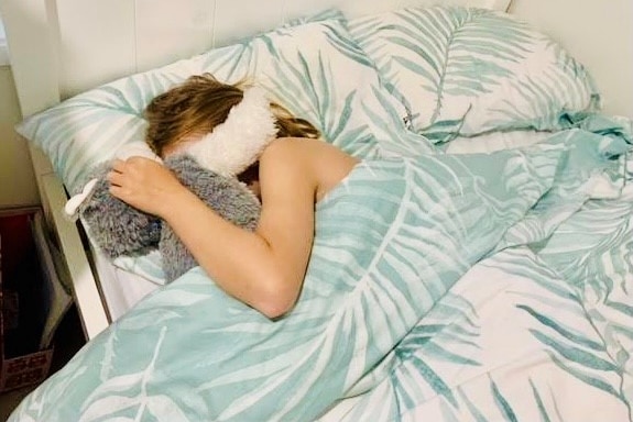 A girl cuddling a teddy asleep in bed
