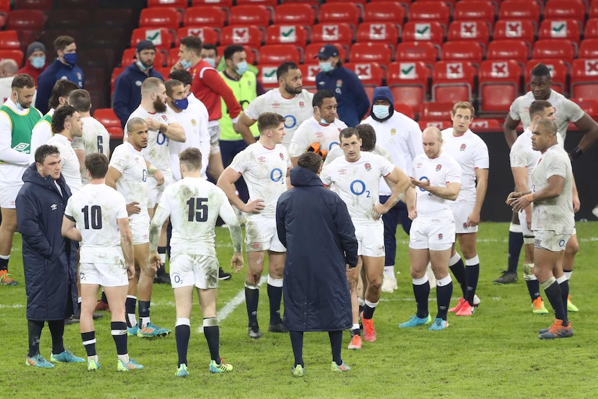 England players stand looking at each other with a background of empty red seats