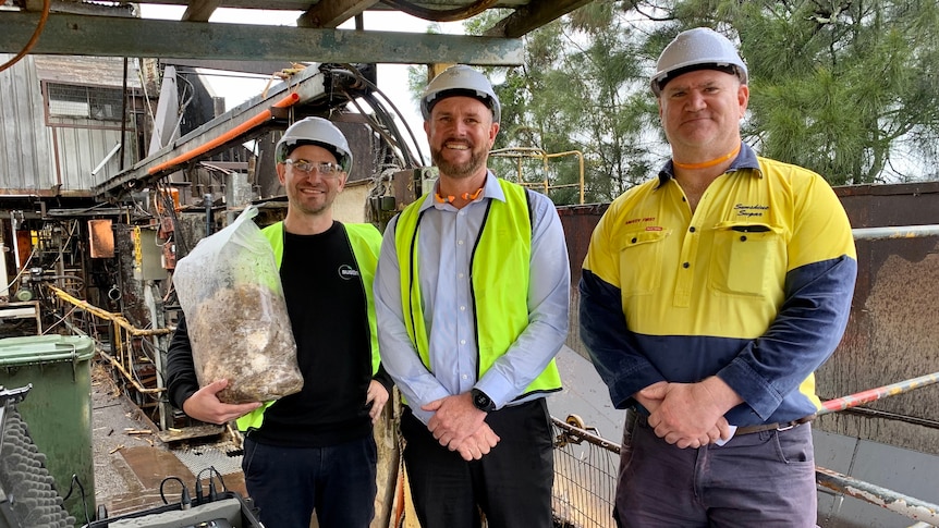 Three men wearing hi-vis shirts and vests and white helmets smiling at camera.