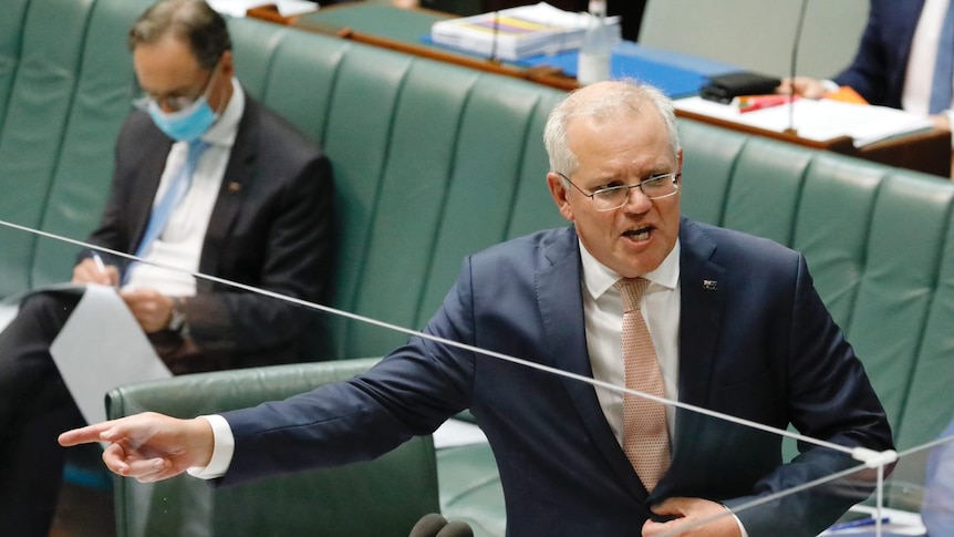 A balding man in glasses buttons up his suit jacket and points while delivering a speech in the House of Representatives.