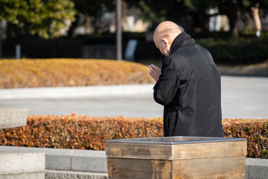 A man with his head bowed in prayer in a park
