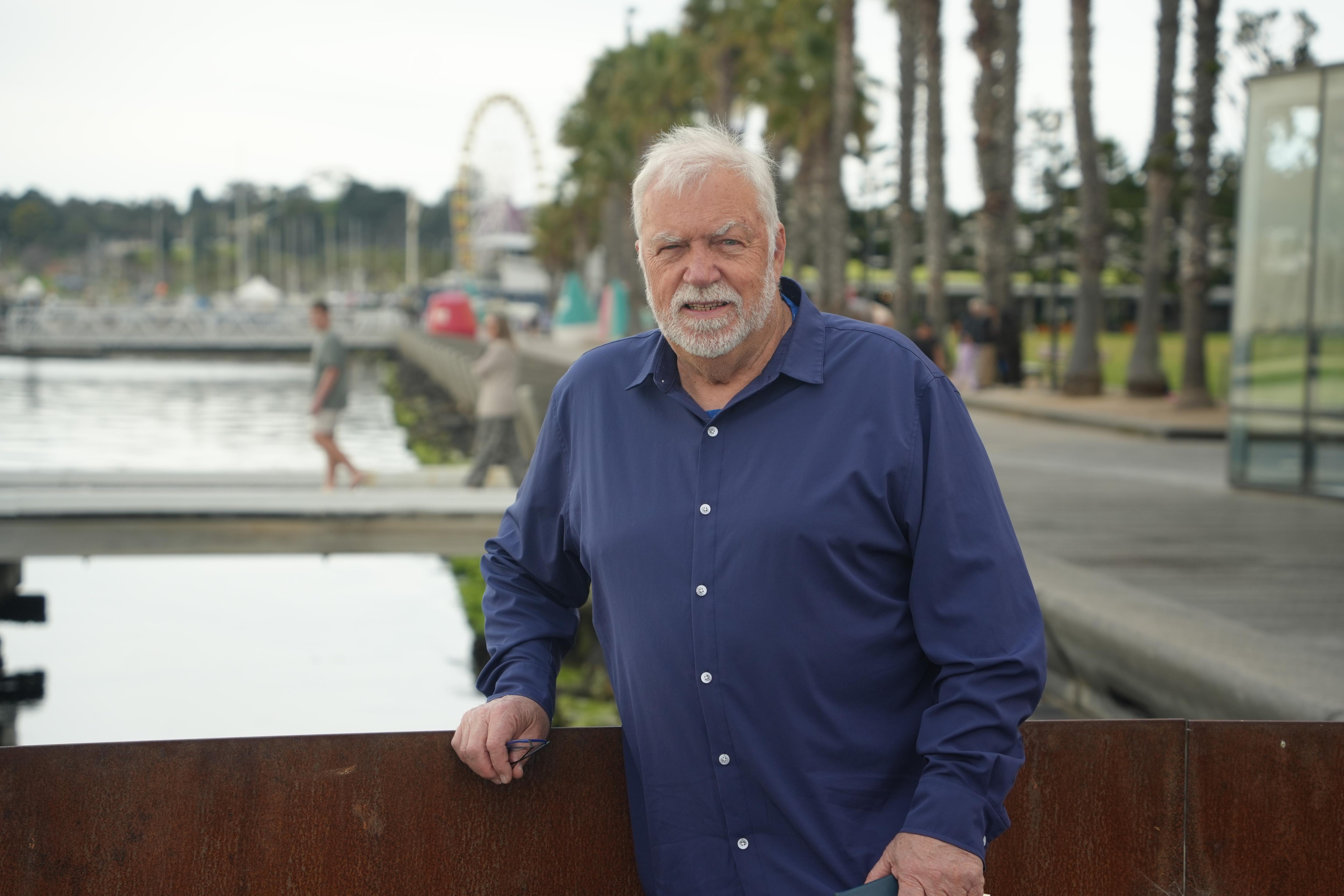 A white-haired, bearded man in an open-necked navy blue shirt stands at Geelong waterfront.