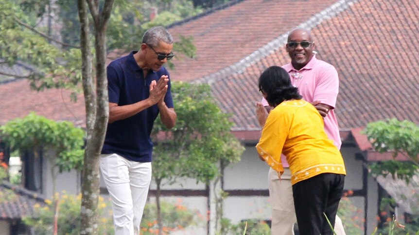 barack Obama wears a navy polo shirt and white pants as he bows in respect to staff during a visit to an Indonesian temple