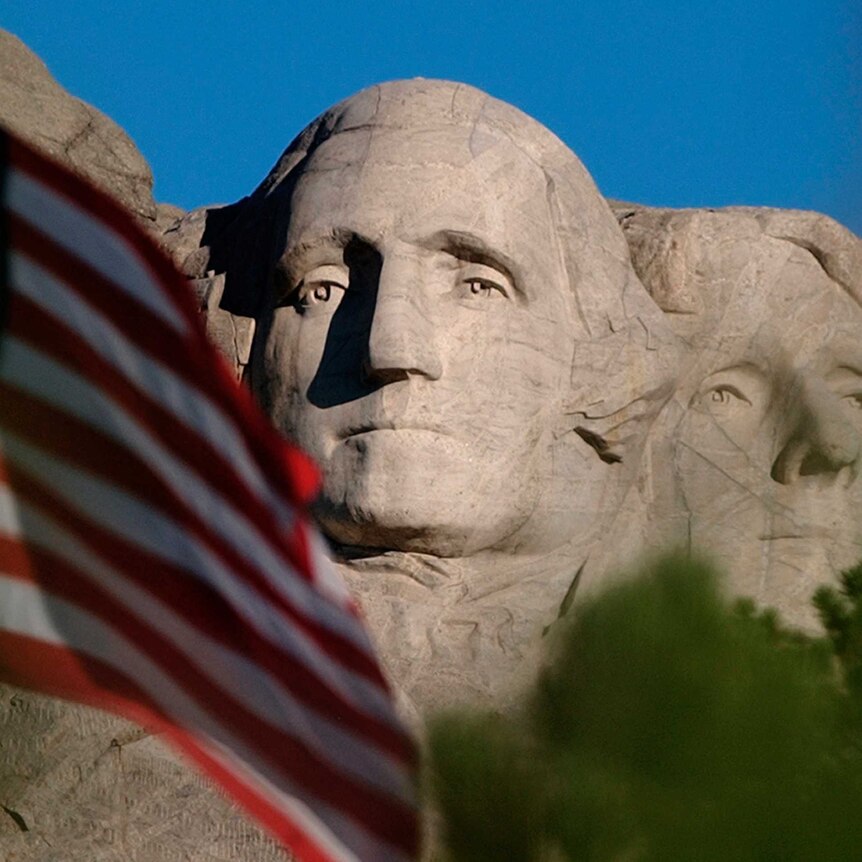 A US flag flies in front of the stone faces carved on Mt Rushmore in the United States.