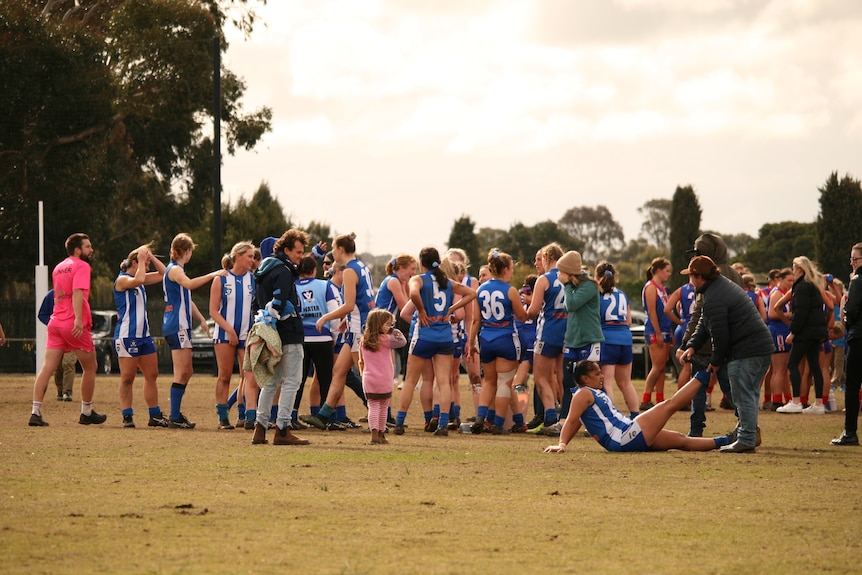 Women in blue and white jumpers on a football ground at dusk