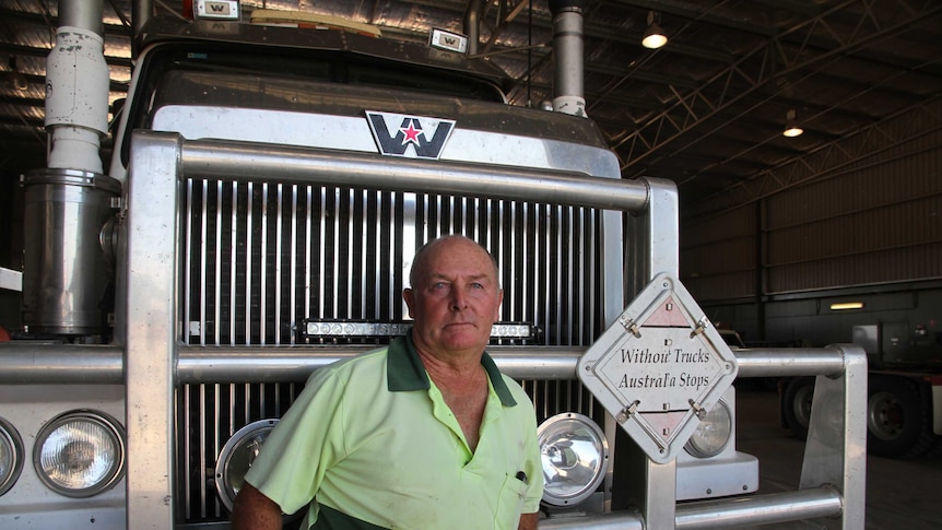 Man leans on a prime mover inside a transport company depot, looking into the camera.