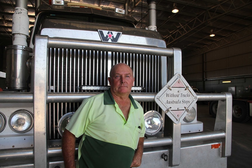 Man leans on a prime mover inside a transport company depot, looking into the camera.
