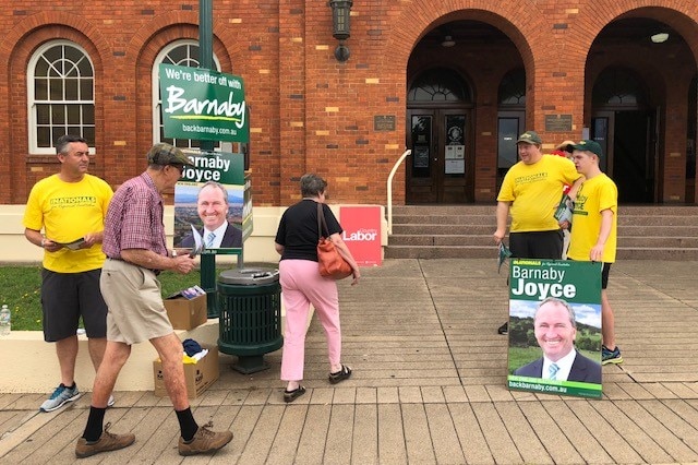 Voters walk past Nationals supporters in yellow shirts and Barnaby Joyce signs towards a polling booth