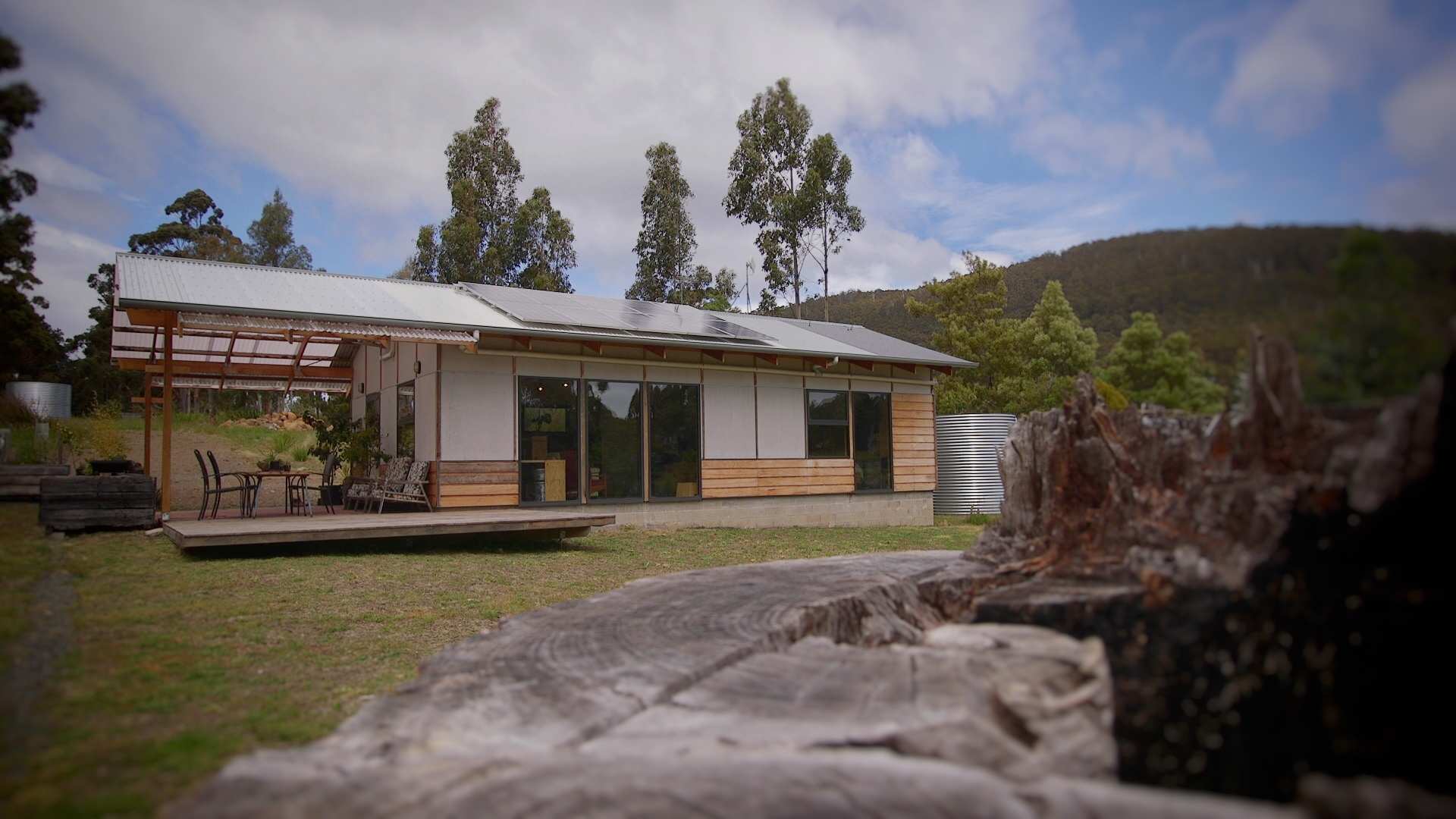 A home in a rural setting with solar panels, a rainwater tank and a deck with patio furniture