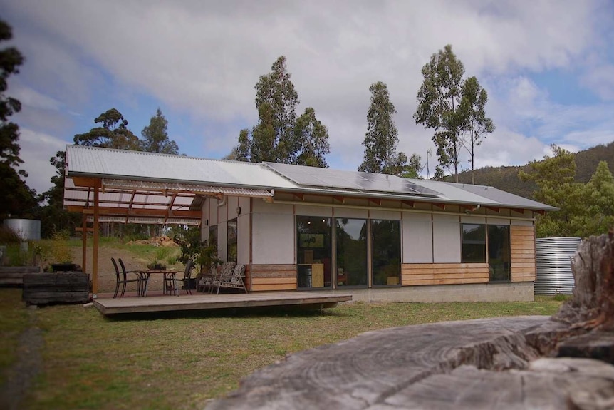 A home in a rural setting with solar panels, a rainwater tank and a deck with patio furniture