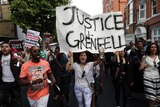 Woman stands under large sign that reads "Justice for Grenfell.