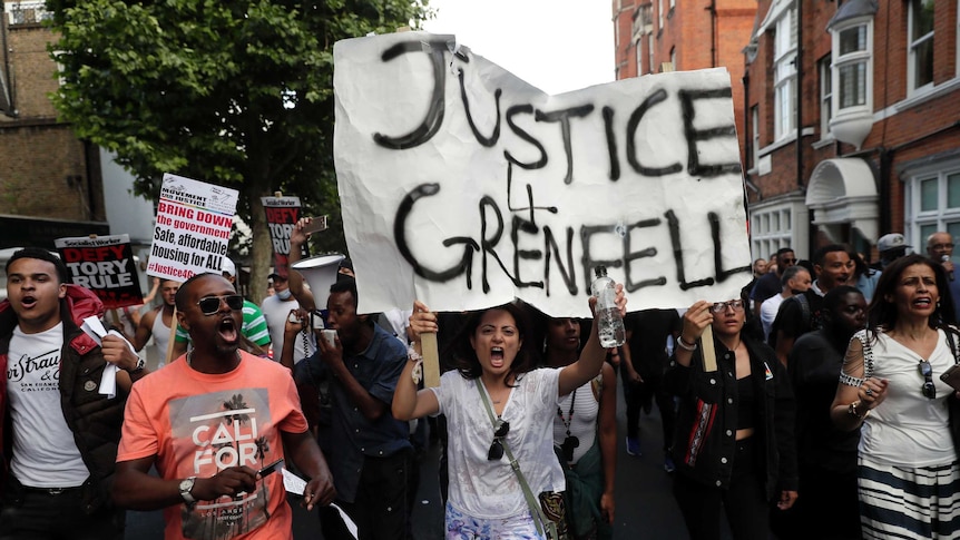 Woman stands under large sign that reads "Justice for Grenfell.