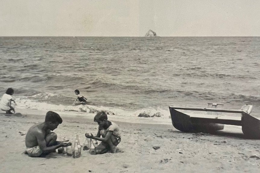 Man and boy crouched on beach holding glass bottles